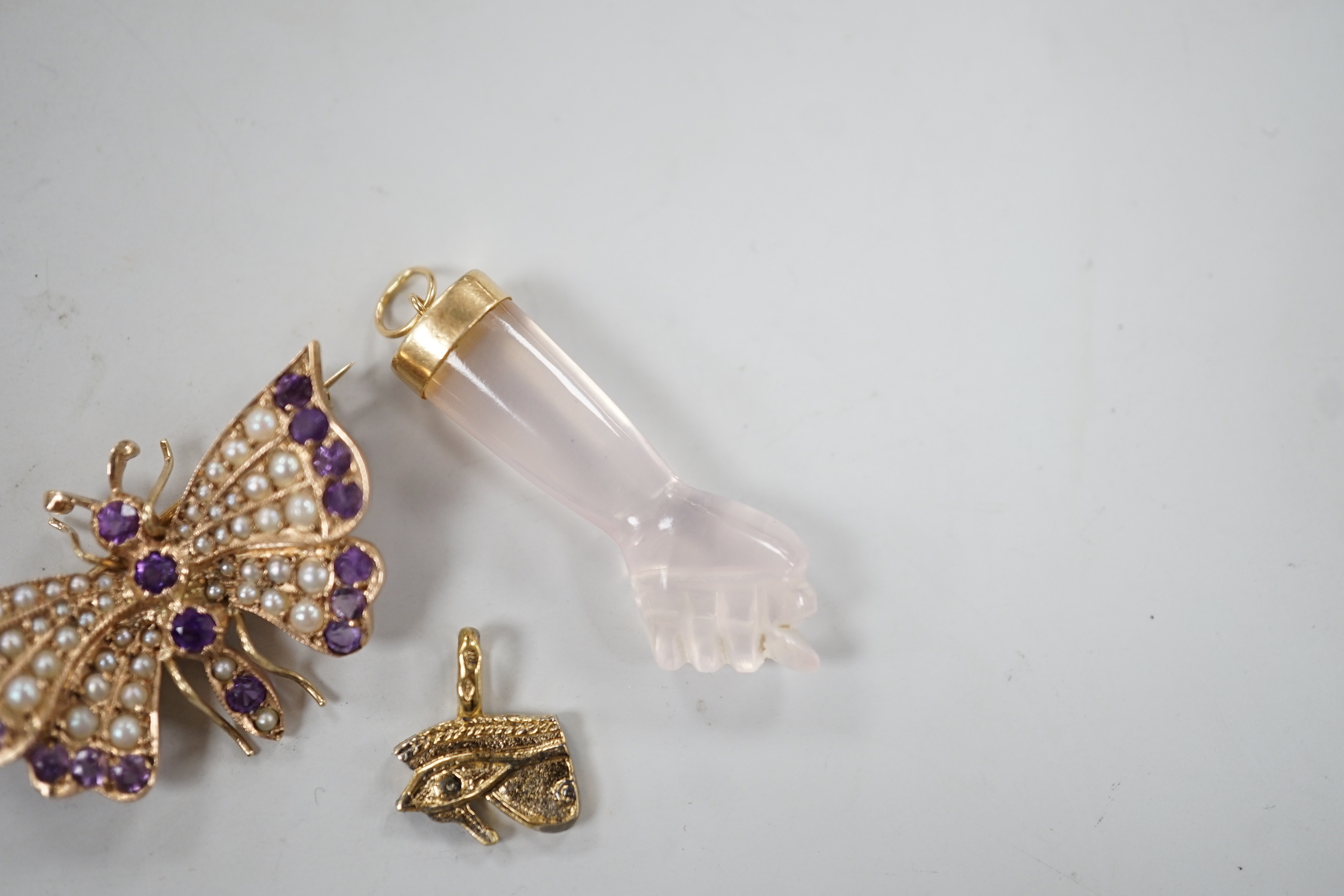 A modern 9ct gold, amethyst and seed pearl cluster set butterfly brooch, width 32mm, together with two charms including arm and fist.
